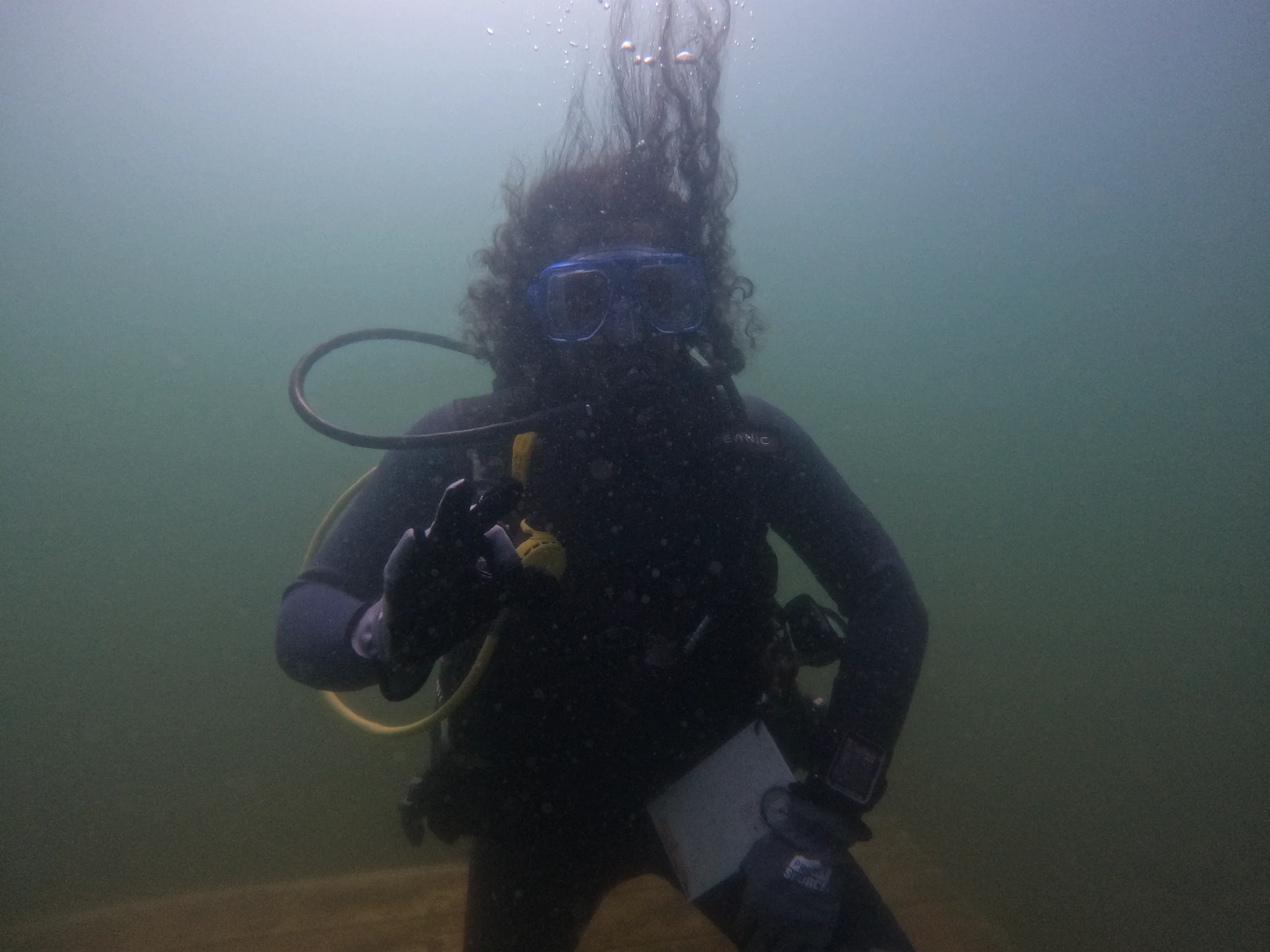 Arjun underwater in scuba gear, facing the camera and making an okay hand signal.